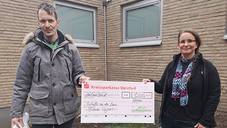 Zwei Personen mit übergroßem Scheck in der Mitte